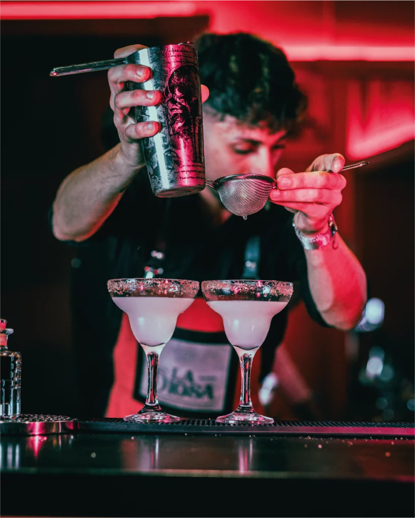 Bartender che versa cocktail in due bicchieri con bordo zuccherato al La Diosa.