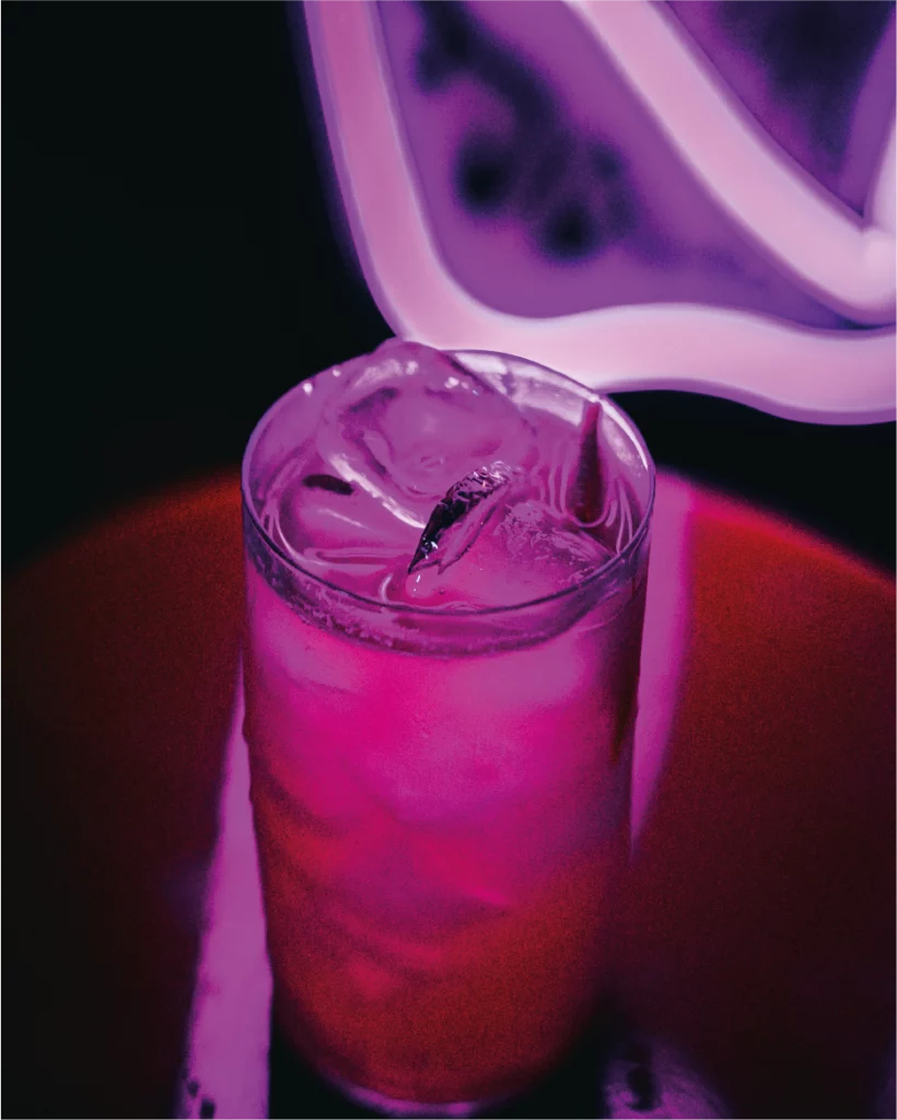 Cocktail rosa servito davanti a un'insegna luminosa al La Diosa.